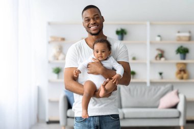 Babalık kavramı. Mutlu genç bir adamın portresi yeni doğmuş şirin bir bebeği elinde tutarken ve kameraya bakarken gülümseyen bir milenyum babasının evde bebeğiyle bağ kurması ve uzay kopyalaması.