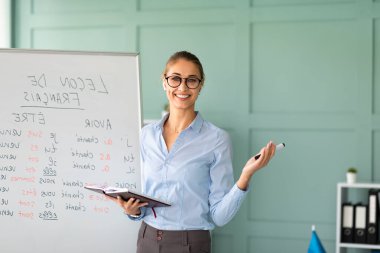 Neşeli bir öğretmen beyaz tahtanın yanında dururken Fransızca dil kavramları hakkında bilgi paylaşıyor. Sınıf misafirperver ve öğretmen dil öğrenmeyi teşvik etmek için heyecanlı..