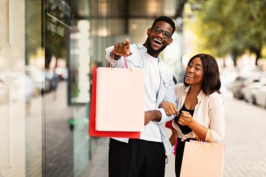 Harika bir teklif. Heyecanlı genç Afrikalı eşler kaldırım kenarında parlak alışveriş torbalarıyla dikiliyorlar. Duygusal adam mağazanın camını işaret ediyor. Çift mevsimlik indirimlerden ve anlaşmalardan zevk alıyor.