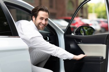 Pozitif yüz ifadesi, başarılı bir alışveriş, kiralık ve test sürüşü. Beyaz arabalı genç, çekici, neşeli Avrupalı adam kapıyı açıyor ve kameraya bakıyor, boş alan, maket.