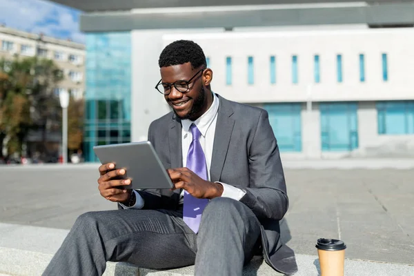 Mutlu Afro-Amerikan isyancı ajanı tablet üzerinde çalışıyor, bloknotlarda haberlere bakıyor, şehir merkezindeki modern ofis merkezinin yakınında oturuyor,