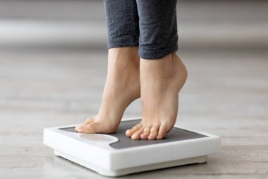 Kapalı alanda ağırlığını ölçen, terazinin üzerinde duran genç Hintli bir kadın. Tanımlanamayan milenyum hanımefendisi zayıflama sürecinin sonuçlarını kontrol ediyor.