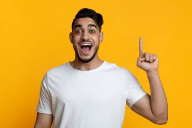Duygusal, genç, yakışıklı Arap adam parmağını kaldırıyor ve çığlık atıyor, sarı stüdyo arka planında 