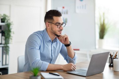 İş yerindeki bilgisayarlı bilgisayarı kullanan pozitif Arap işadamı, web kamerasından iş arkadaşlarıyla konuşuyor. Başarılı bir milenyum ofis çalışanı önemli belgeyi çevrimiçi okuyor, e- postaları kontrol ediyor