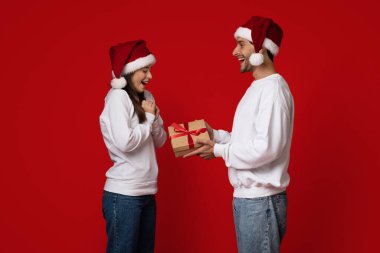 Neşeli bir an, Noel hediyelerini paylaşan neşeli bir çifti yakalar. Her ikisi de Noel Baba şapkası takıyor ve gülümsüyor..