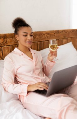 Genç Afro-Amerikalı kadın dizüstü bilgisayar kullanarak yatakta oturuyor ve güzellik bakımından sonra şaraptan zevk alıyor, internette sörf yapıyor ya da arkadaşlarıyla konuşuyor. Pembe ipek giysili kadın evde bilgisayarla dinleniyor.