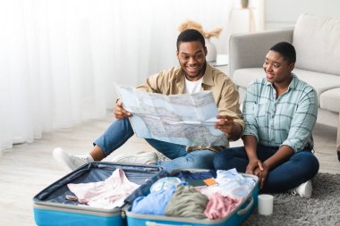 Seyahat Konsepti. Afro-Amerikalı Gezginler Turistik Tatil Yeri Evdeki Oturma Odasında Oturan Bavulun Yakınındaki Haritayı Seçiyor. Eşler Bir Sonraki Yolculuğu Birlikte Planlıyor