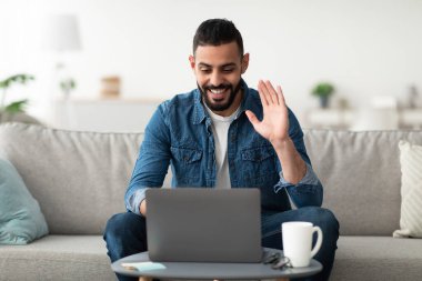 Çevrimiçi toplantı. Konferans için dizüstü bilgisayar kullanan mutlu genç bir Arap. Evde video görüşmesi yapıyor. Milenyum Doğulu bir adam meslektaşlarıyla ya da arkadaşlarıyla uzaktan iletişim kuruyor.