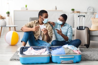 Seyahat Başvurusu. Siyahi turistler akıllı telefon çantalarını evde birlikte kullanıyor, maske takıyorlar. Eş Gezginlere Tatile Hazırlık İçin Harika Uygulama Öneriyor