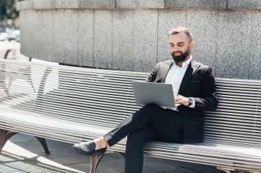 Kapalı alan 19 'daki tecrit sırasında uzaktan kumanda. Kendine güvenen yetişkin iş adamı ya da takım elbiseli yönetici dışarıda ofis merkezinin yanındaki bankta otururken dizüstü bilgisayar kullanıyor, boşluğu kopyala