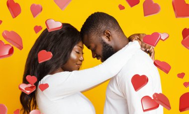 Genç evli çift, kalp grafikleriyle çevrili bir şekilde birbirlerine gülümseyerek sarılıyorlar. Aşkları, sarı bir zemin ile basit bir stüdyo ortamında ışıldıyor..