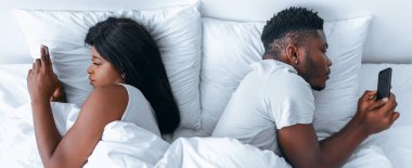 İki kişi beyaz çarşaflı bir yatakta yatıyor. Birbirlerine bakmıyorlar, her biri kendi telefonuna bakıyor. Oda basit ve parlak, aralarındaki mesafeyi vurguluyor..