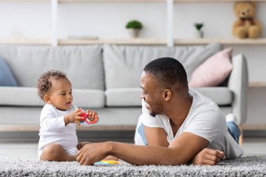 Ortak ebeveyn izni. Genç siyah baba evde küçük bebekle oynuyor, mutlu Afrikalı Amerikalı adam sevimli bebeğiyle oturma odasında vakit geçiriyor, babalığının tadını çıkarıyor, boşluğu kopyalıyor.