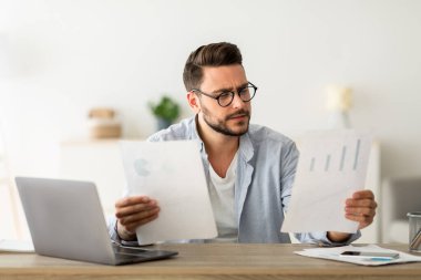 Uzaktan kumanda. Evraklar ve dizüstü bilgisayarlarla çalışan meşgul bir erkek girişimci. İş yerinde otururken mali raporları kontrol eden yakışıklı bir adam