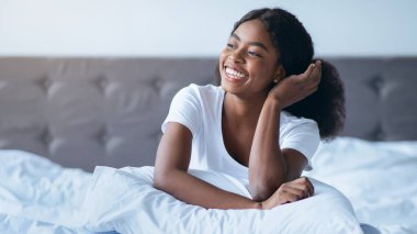 İyi aydınlatılmış bir odada beyaz çarşaflı bir yatakta oturan bir insan. Yastığa sarılmış halde gülümsüyor ve saçlarıyla oynuyorlar. Sabah ışığı pencereden parlıyor..