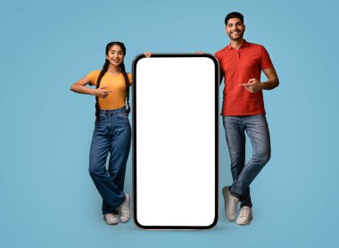 İki genç insan büyük bir akıllı telefon ekranının yanında dururken gülümsüyor. Sahnede açık mavi bir arkaplan, onların dost duruşu ve modern stili vurgulanıyor..