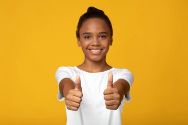 Beyaz tişörtlü Afro-Amerikan öğrenci kız öğrencisinin sarı arka planda izole edilmiş el hareketleriyle baş parmak hareketi yapması tatmin ediciydi. Başarı, havalı işaret konsepti, olumlu duygular
