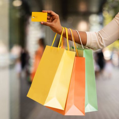 Modern Alışveriş, Temassız Ödeme, Satış sezonunda İndirim. Binlerce yıllık Afro-Amerikan kadının elinde bir sürü renkli alışveriş torbası ve kredi kartı, bulanık bir arka plan, seçici bir odak