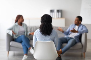 Evlilik terapisi. Ofiste mutsuz siyah bir çiftle olan randevusu sırasında kameraya arkası dönük oturan profesyonel psikolog, seçici bir odak. Psikoterapist, genç bir ailenin sorunları çözmesine yardım ediyor