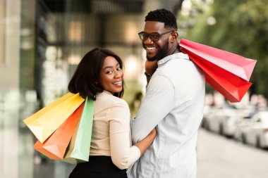 Satış ve Tüketim Konsepti. Alışveriş torbası tutan mutlu Afro-Amerikan çiftin portresi. Gülümseyen siyah adam ve kadın alışverişleri taşıyor, arkasını dönüyor ve kameraya bakıyor.