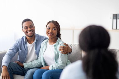 Evlilik danışmanlığında başarılı bir psikoterapiden sonra mutlu bir çift. Olumlu genç siyah eşler psikologlarıyla sonuçları paylaşıyor, klinikteki kanepede sarılıyorlar.