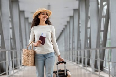 Tatil seyahati. Havalimanı Terminalinde Wicker Şapkalı Güzel Esmer Kadın, Mutlu Gülümseyen Milenyum Kadını Tatil Gezisine Hazır, Ayrılış Kapısına Gidiyor, Kopya Boşluğu