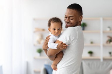 Mutlu Milenyum Siyah Babası, tatlı bebeğiyle evde vakit geçiriyor, Afrikalı Amerikalı babasını seviyor, sevimli küçük çocuğunu taşıyor ve gülümsüyor, babalık izninin tadını çıkarıyor, boşluğu kopyalıyor.