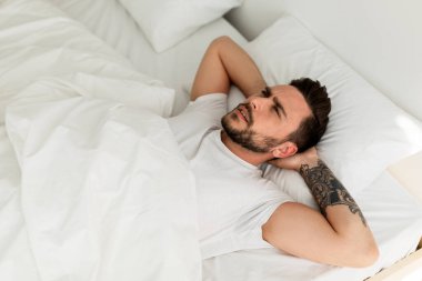 Kızgın genç adam uyuyamıyor, uykusuzluk çekiyor, yatakta uzanıyor ve yukarı bakıyor, uzayı kopyalıyor. Akıl sağlığı sorunu, erkek depresyonu ve uykusuzluk kavramı