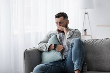 Olumsuz duygular yüzünden hayal kırıklığına uğramış, mutsuz erkek, problem çözmeyi düşünüyor, orta yaş krizi yaşıyor. Bin yıllık yakışıklı, kaslı, sakallı adam kanepede oturup iç mekanda ağlıyor.