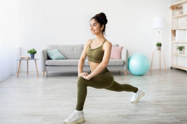 Güzel Hintli genç bayan hamlesini yapıyor, güç egzersizleri yapıyor, evde kalça ve bacak kaslarını çalıştırıyor, tam boy. Mutlu Asyalı kadın idman yapıyor, covid sırasında aile sporları yapıyor.