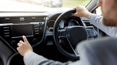 Yeni araba kullanan adam koltukta oturur, modern otomobilde direksiyon tutar. Milenyum Kafkasyalı takım elbiseli adam gösterge panelinde müzik değiştiriyor, şehre giderken teknoloji kullanıyor, panorama, kesilmiş...