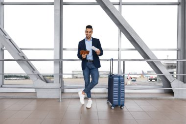 Havalimanında uçuşunu bekleyen yakışıklı Orta Doğulu erkek gezginin portresi, Terminal 'de pencerenin yanında duran gülümseyen genç bir Arap, hava yolculuğuna hazır pasaport ve biletleri kontrol ediyor.