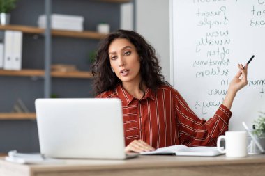 Öğrenme Kavramı. Ciddi bir bayan öğretmenin, bilgisayar kullanarak görüntülü görüşme yaptığı portresi. Kablosuz kulaklıklı bir bayan, webcam 'e konuşuyor, öğrencilere özel ders veriyor.
