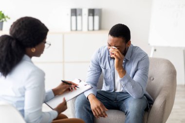 Depresyondaki siyah adam klinikte profesyonel yardım almak için psikoterapistlerin ofisinde ağlıyor. Profesyonel psikolog mutsuz bir erkek hastayla terapi seansı yapıyor.