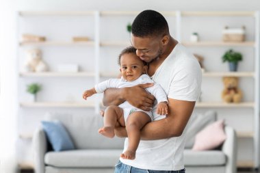 Baba ve Çocuk. Mutlu Afrikalı Amerikalı bir babanın portresi, ellerinde şirin bir erkek bebek, iç mekanda birlikte poz veriyor, sevimli siyah çocuk kameraya bakıyor ve gülümsüyor, boşluğu kopyalıyor.