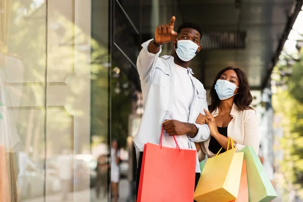 Hadi bunu alalım. Tıbbi maske takan Afro-Amerikan bir adamın portresi dükkan camını işaret ediyor, koca alışveriş merkezinin yakınında karısıyla birlikte alışveriş çantalarını tutuyor. Mevsimlik Satış ve İndirim