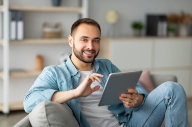 Çevrimiçi yaşam konsepti. Mutlu genç adam tablet bilgisayar kullanıyor, çalışıyor ya da evde çalışıyor. Yakışıklı beyaz adam Webinar ya da internet konferansına katılıyor, iş görüşmesi yapıyor.