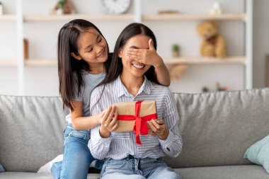 Neşeli Asyalı kız, mutlu annesi için sürpriz yapıyor, gözlerini kapayıp hediye kutusu veriyor ve evdeki kanepede oturup, fotokopi çekiyor.