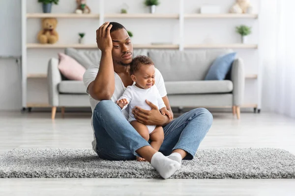 Blues Baba. Stresli genç siyah baba evde yerde ağlayan bebekle oturuyor, üzgün Afrikalı Amerikalı baba kafasına dokunuyor, ızdırap çeken babalık sorunları yaşıyor, kopyalama boşluğu dolduruyor.
