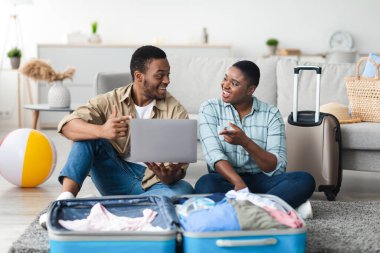 Aile tatili. Afro-Amerikan turistler dizüstü bilgisayarlı rezervasyon biletleriyle evdeki koltukta oturuyorlar. Eş Planlama Gezisi İçerideki Bilgisayarda İnternet Taraması. Seçici Odaklanma