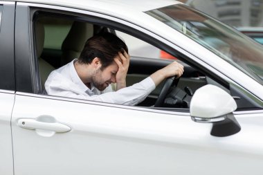 Kendi arabasında trafiğe takılmış, elini alnına koyup gergin bir şekilde bekleyen bir iş adamı. Mutsuz milenyum çekici, beyaz otomobilli üzgün Avrupalı adam şehirde strese girdi.