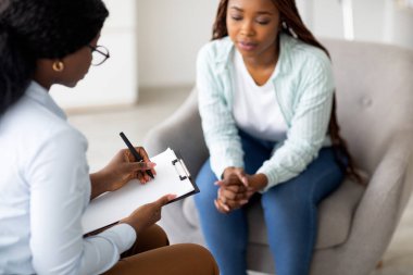 Stresli siyahi kadın hasta danışmanlık psikoloğu, seçici odaklanma. Psikiyatrist, üzgün Afrikalı Amerikalı kadına sinir problemleri konusunda yardım ediyor, seans sırasında not alıyor.