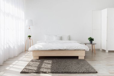 Gerçek fotoğraf. Klasik modern yatak odası ve iç tasarımı olan büyük, rahat, çift kişilik yataklı bir ev. Pencere ışığında mobilyalar, çömlek içinde yeşil bitkiler olan masalar, beyaz duvar