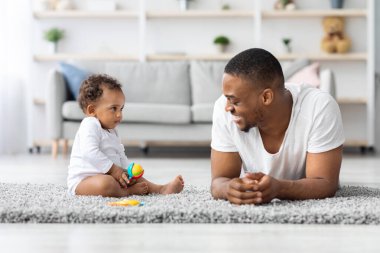 Genç, mutlu, Afrikalı bir babanın evde tatlı bir bebekle oynadığı, siyahi bir babanın sevimli küçük bir çocuğa baktığı, gülümsediği, babalığının tadını çıkardığı, boşluğu kopyaladığı portresi.