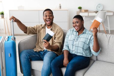 Neşeli Afrikalı turistler, tatilin başlamasını kutlamak için seyahat biletleri tutuyor. Evde koltukta bavullarıyla otururken kameraya gülümsüyorlar. Yeni Trip, sonunda. Seyahat Konsepti