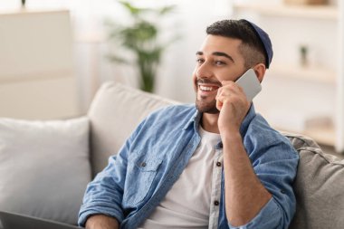Telefon Çağrısı Konsepti. Arkadaşları ya da ailesi ile akıllı telefonda konuşan rahat bir koltukta oturan gülümseyen genç Yahudi 'nin yakın plan portresi. Boş kopya alanı, seçici odak, bulanık arkaplan