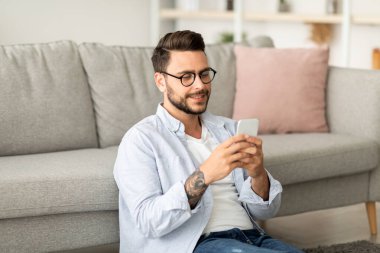 Kullanışlı bir uygulama. Yakışıklı milenyum adamı evde dinlenirken smatphone kullanıyor, yerde oturuyor oturma odasında kanepeye yaslanıyor, fotokopi çekiyor. İnternette gezinen ya da arkadaşlarıyla mesajlaşan adam