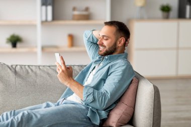 Yakışıklı milenyum çocuğu koltukta cep telefonuyla rahatlıyor, gülümsüyor ve evde arkadaşına mesaj atıyor. Genç beyaz adam mesaj yazıyor, görüntülü konuşma yapıyor ya da evde internet yayıyor.