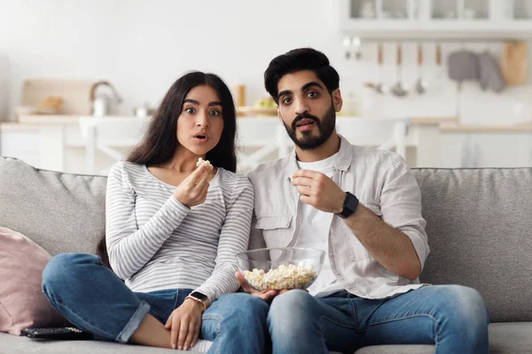 Evdeki korkutucu, ilginç ve heyecan verici sinema ve insani duyguların ifadesi. Şaşırmış genç Arap kadın ve erkek ağızları açık ve patlamış mısırlı oturma odasında televizyon seyrediyor, boşluğu kopyalıyor.