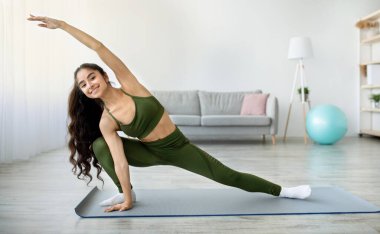 Genç Hintli kadın yoga ya da pilates yapıyor, ev içi eğitim sırasında kollarını ve bacaklarını esnetiyor, fotokopi çekiyor. Sportif Asyalı bayan esnek egzersizler yapıyor, evde sağlıklı bir yaşam sürüyor.
